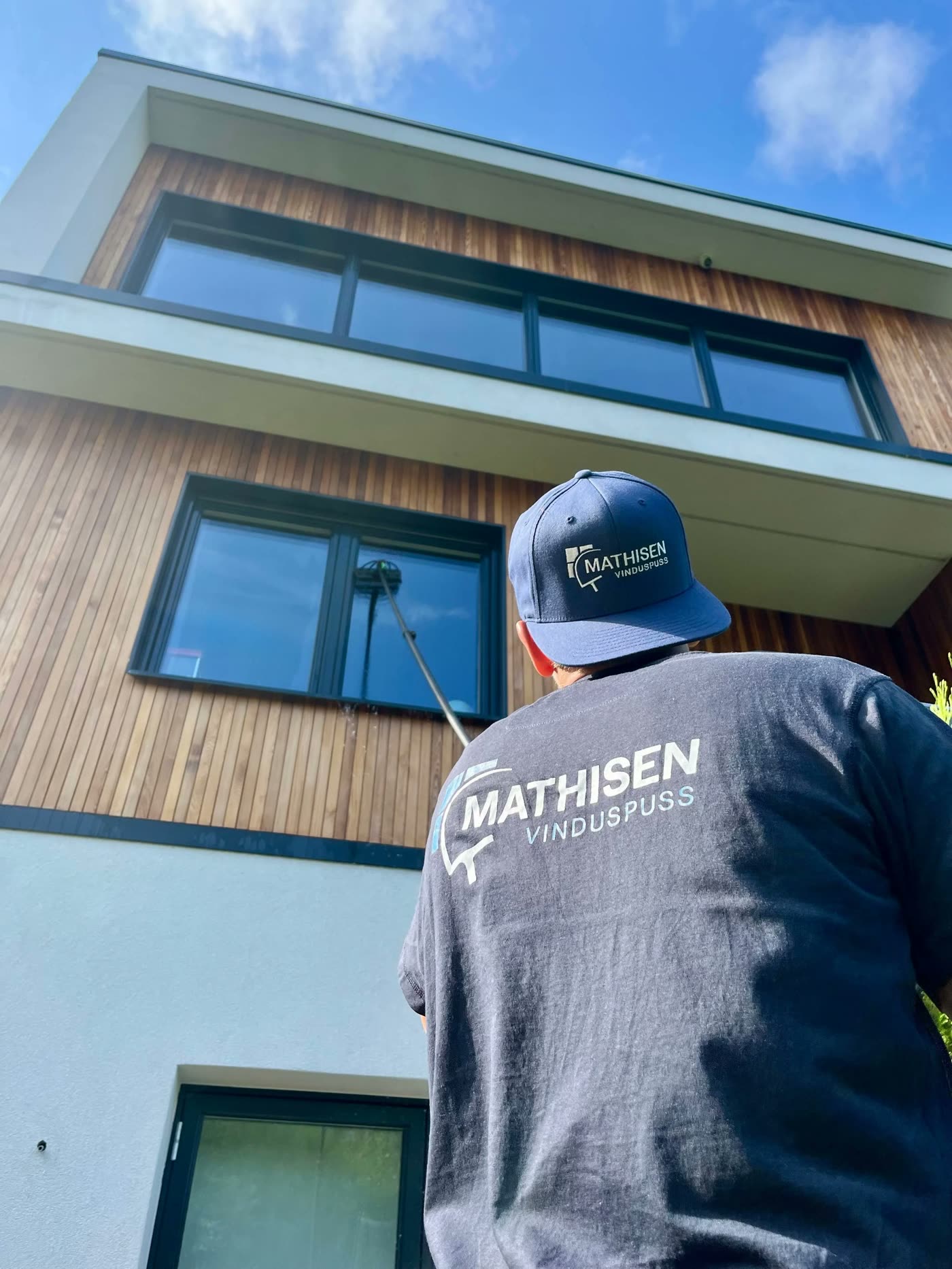 Ansatt fra Mathisen Vinduspuss pusser vinduene i andre etasje på en enebolig med stang fra bakken